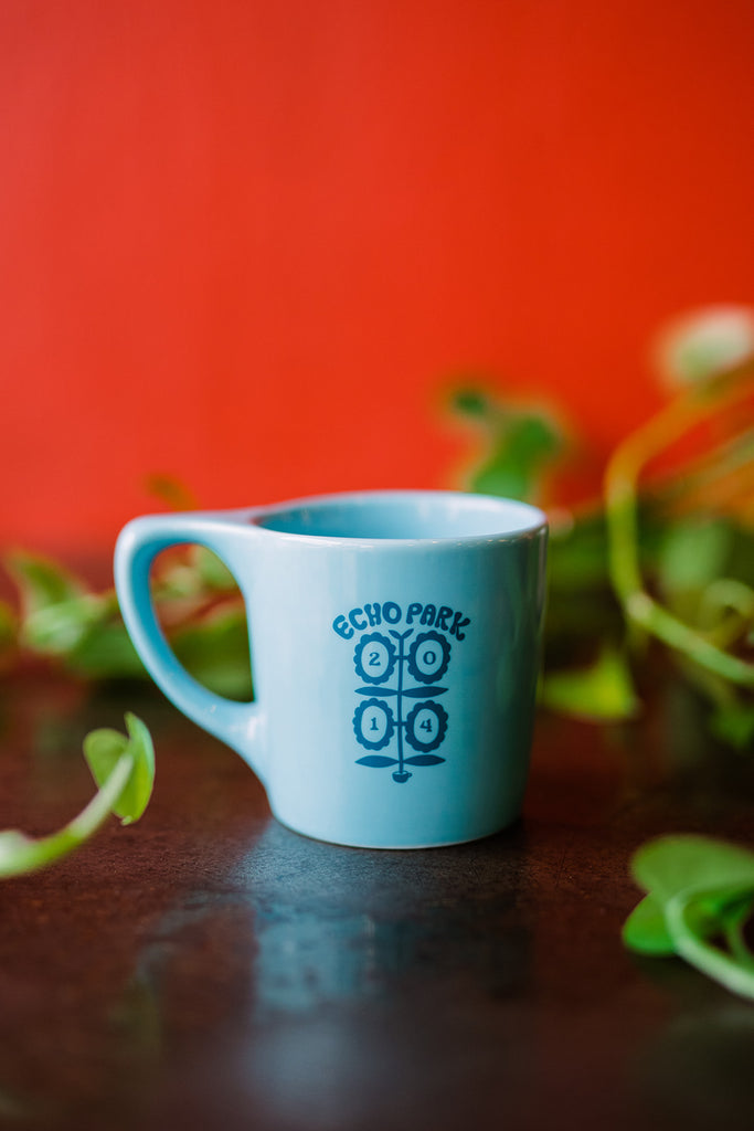 A blue coffee mug with a darker blue illustration that reads "echo park" in an arched shape on top of flowers