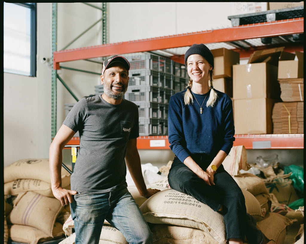 A photo of a smiling man and woman sitting atop a palette of burlap sacks
