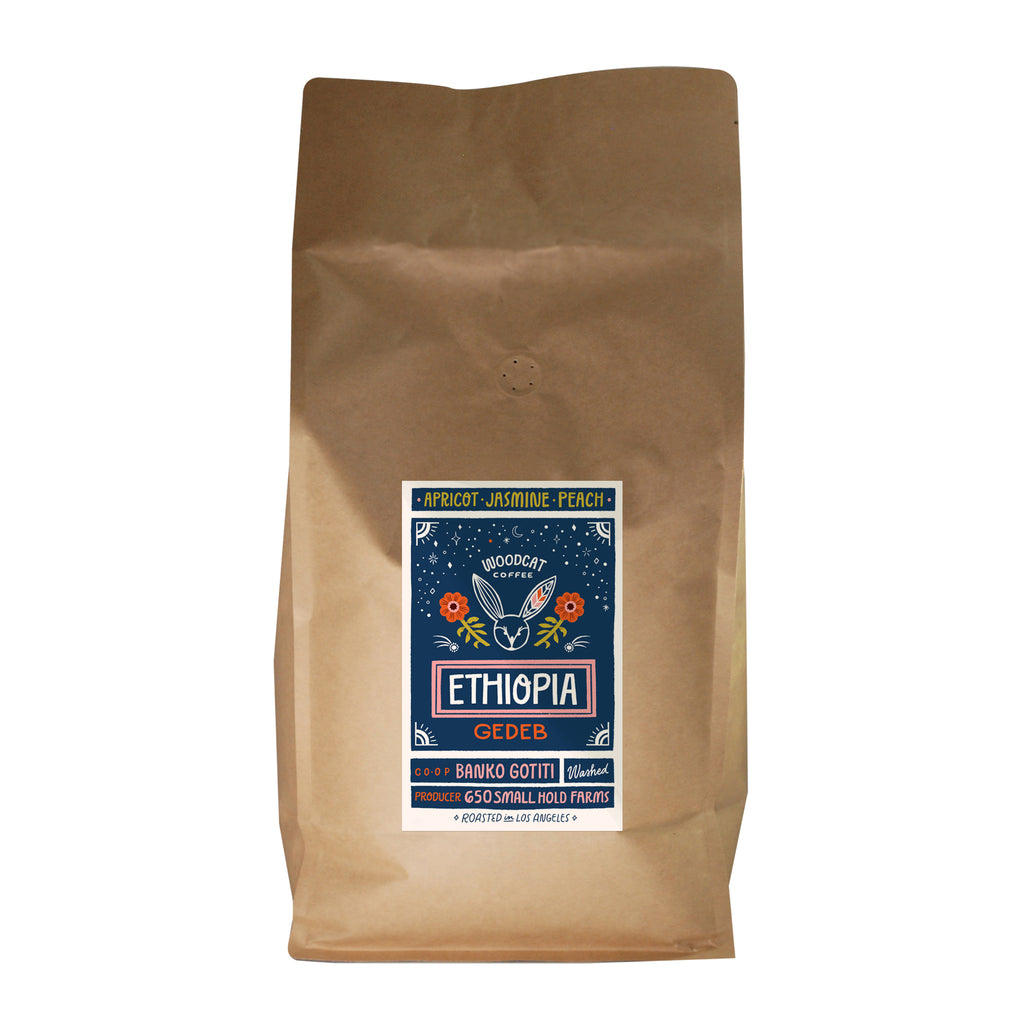 A large brown coffee bag with a blue label that reads "Apricot, Jasmine, Peach. Woodcat Coffee. Ethiopia Gedeb"