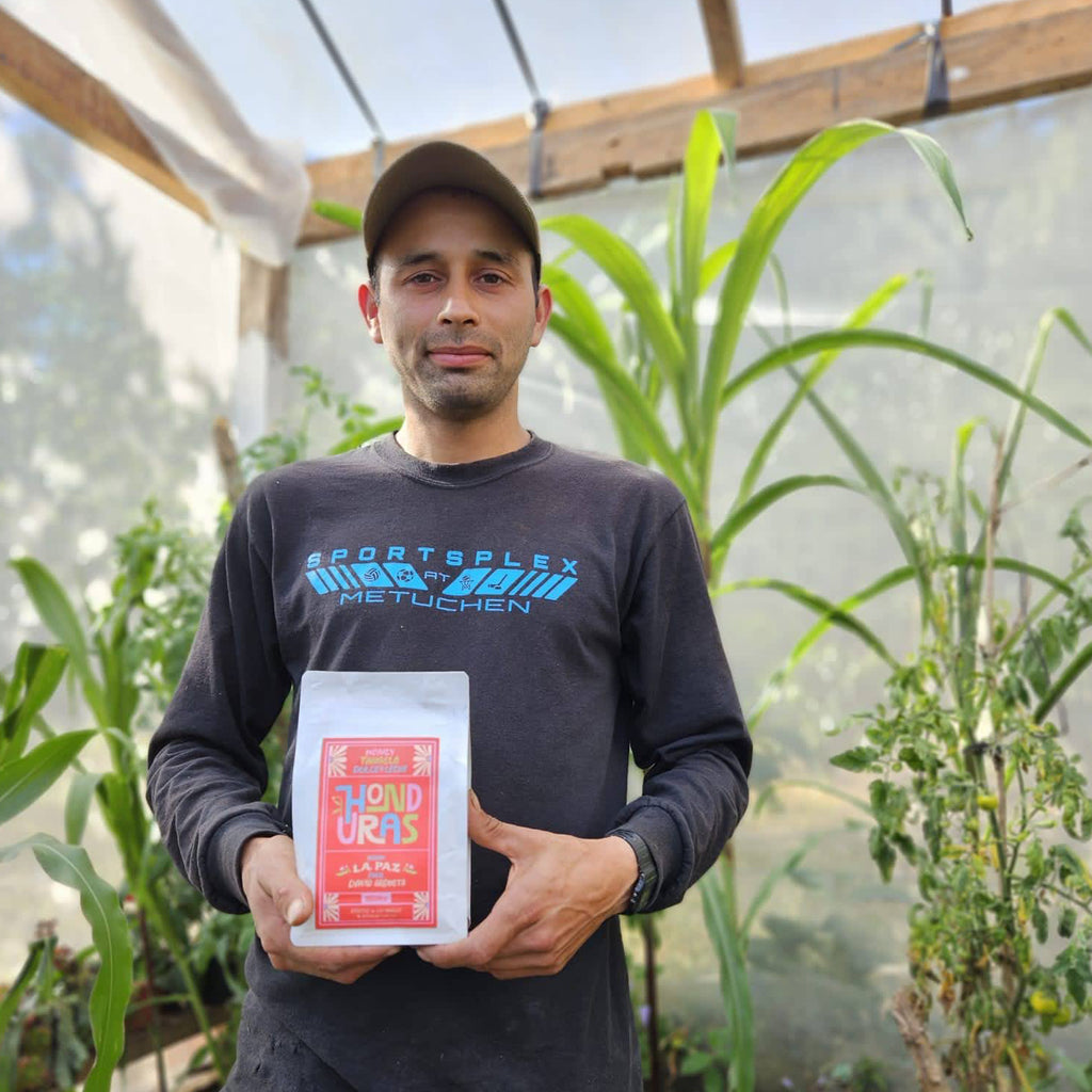 A photo of a man in a black shirt holding a white bag of coffee beans that reads "honduras" in colorful letters