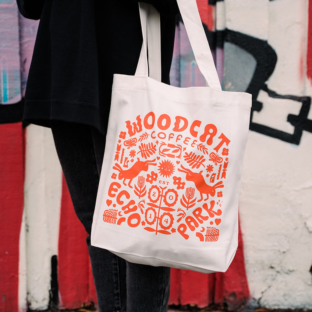 a white tote bag with orange design hanging off a close up right arm
